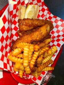 French fries, fried fish and a lemon atop a red and white checkered parchment from Captain's Galley