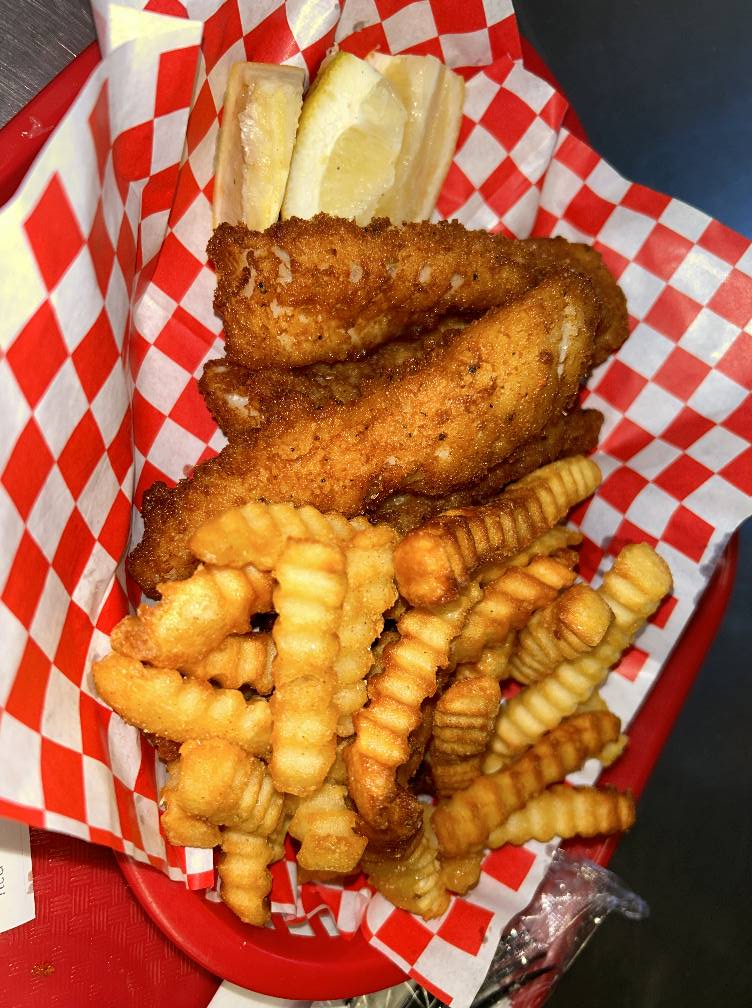 French fries, fried fish and a lemon atop a red and white checkered parchment from Captain's Galley