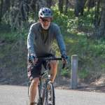 A man wearing a bike helmet rides his bike along a grass-lined trail