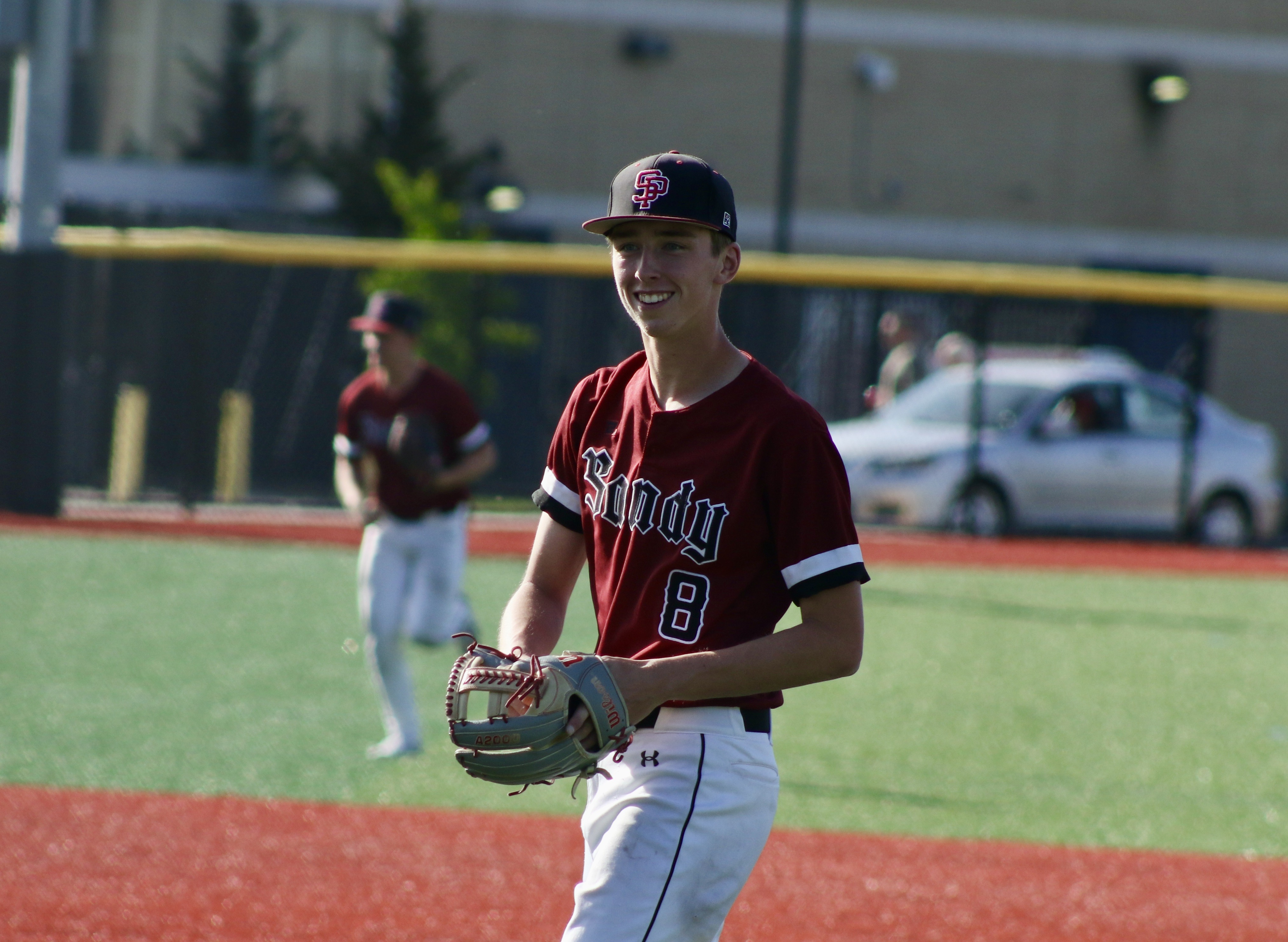 Sandy baseball player Brayden Sievertsen, wearing a red jersey, smiles on the baseball field