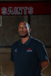 Hany Doud stands with arms behind his back in the Mt. Hood Community College gym in a black polo shirt with the school logo in the top left corner