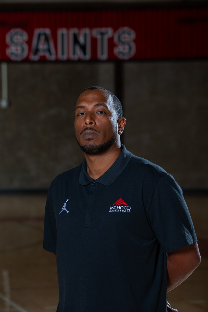 Hany Doud stands with arms behind his back in the Mt. Hood Community College gym in a black polo shirt with the school logo in the top left corner