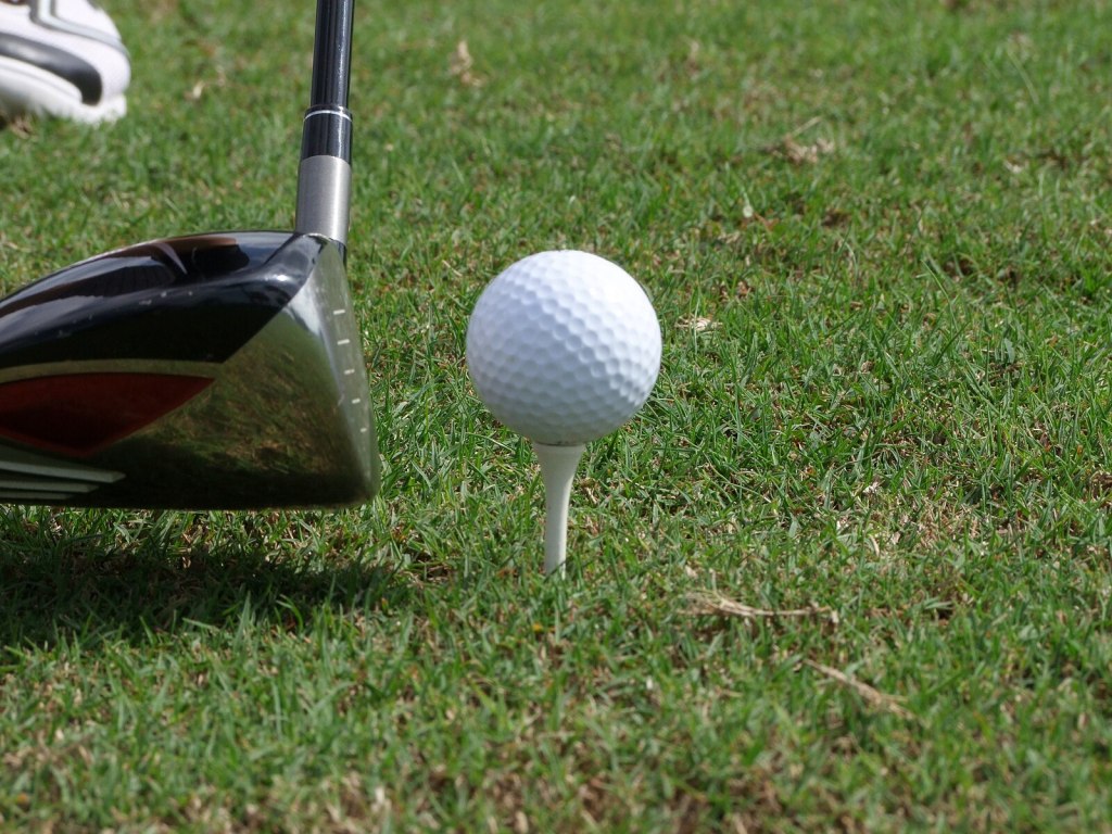 A golf ball sits on a tee in the grass with a driver lining up a shot to the left