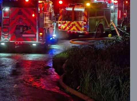 Corbett Fire engines have lights flashing at night while responding to a fire, with hoses stretching off the right of the frame