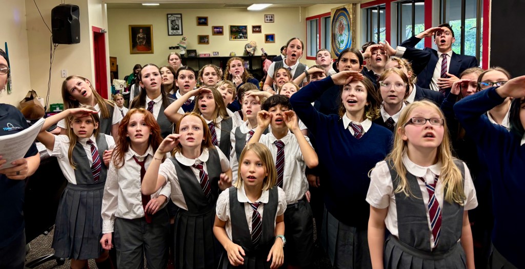 The Eastside Theater Company kid actors of Matilda the Musical stand in a group, wearing their gray school costumes