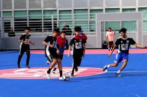 Kids play futsal on a blue outdoor synthetic court