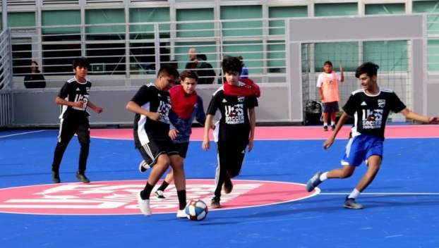 Kids play futsal on a blue outdoor synthetic court