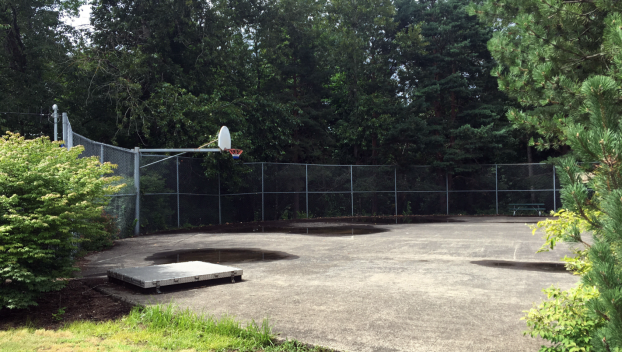 A weathered basketball court with partial fencing atop a concert in-ground reservoir
