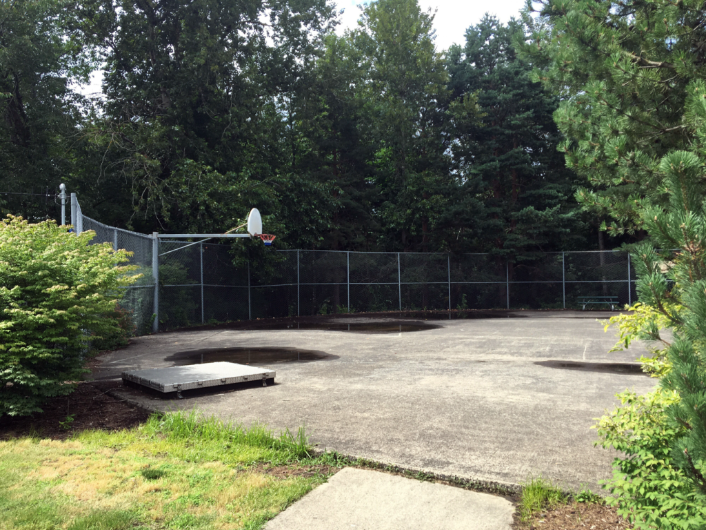 A weathered basketball court with partial fencing atop a concert in-ground reservoir
