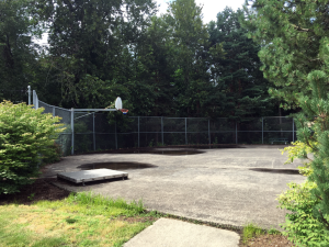 A weathered basketball court with partial fencing atop a concert in-ground reservoir