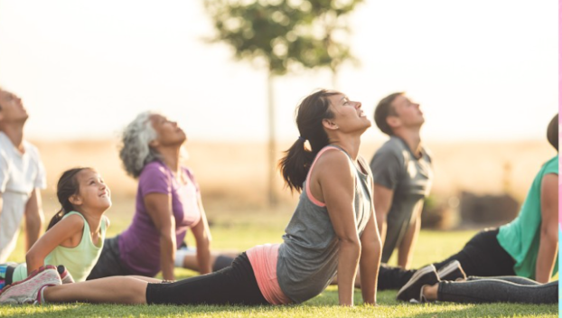 People of all ages do a yoga pose outdoors in a park.