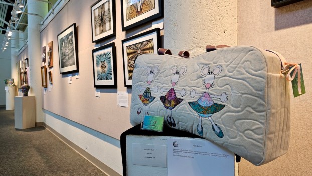 A GALA art exhibit inside Gresham City Council Chambers featuring an ornate bag on a pedestal in front of a wall of paintings
