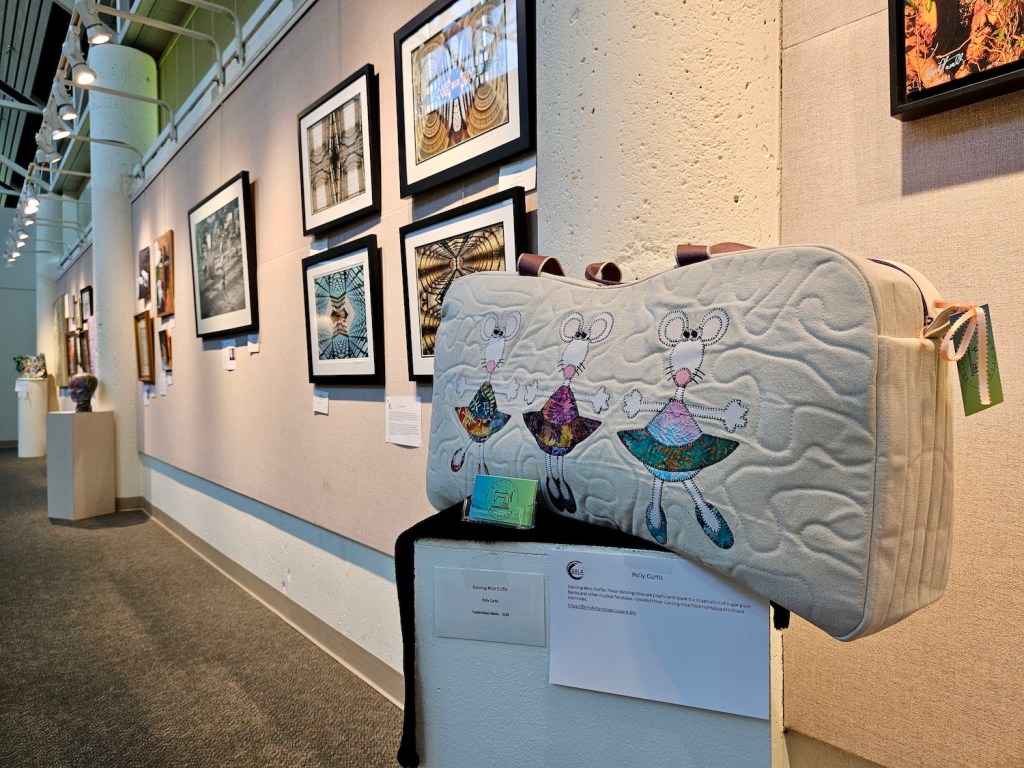 A GALA art exhibit inside Gresham City Council Chambers featuring an ornate bag on a pedestal in front of a wall of paintings