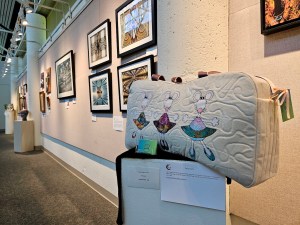 A GALA art exhibit inside Gresham City Council Chambers featuring an ornate bag on a pedestal in front of a wall of paintings