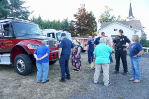 Folks gather in a lot during the Springwater Grange National Night Out celebration. There are firefighters and a fire engine with them