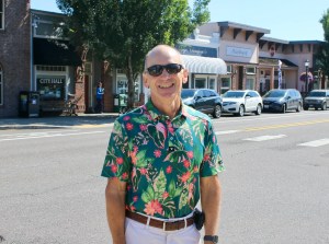 Outgoing Troutdale city manager Ray Young stands in a colorful shirt and sunglasses on a sunny day next to the Historic Columbia River Highway through Downtown.